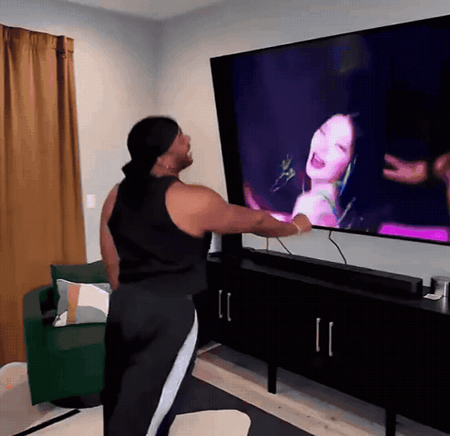 A Woman Is Standing In Front Of A Large Television Screen GIF