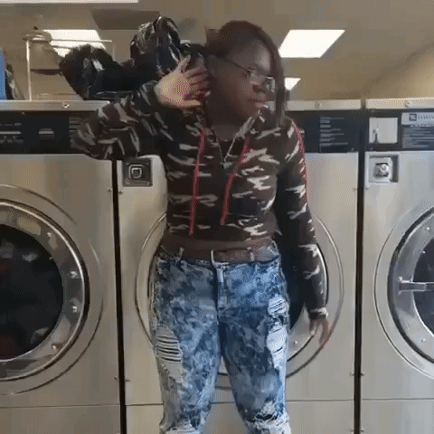 A Woman Is Standing In Front Of A Laundromat Machine With A Sign That Says Warning GIF