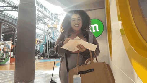 A Woman Is Standing In Front Of A M & M Sign GIF