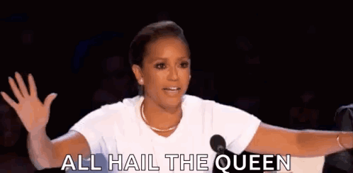 A Woman Is Standing In Front Of A Microphone And Saying `` All Hail The Queen '' While Waving Her Hand . GIF