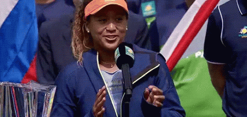 A Woman Is Standing In Front Of A Microphone And Smiling While Wearing An Orange Hat . GIF