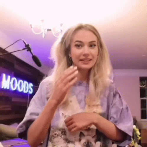 A Woman Is Standing In Front Of A Microphone In A Room With A Sign That Says Moods . GIF
