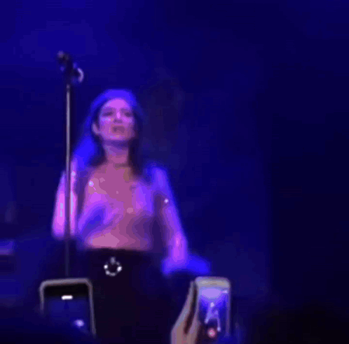 a woman is standing in front of a microphone on a stage while a fan takes a picture of her .
