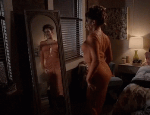 A Woman Is Standing In Front Of A Mirror In A Bedroom GIF