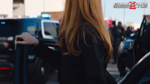 A Woman Is Standing In Front Of A Police Car With The Words Snake Eyes Behind Her GIF