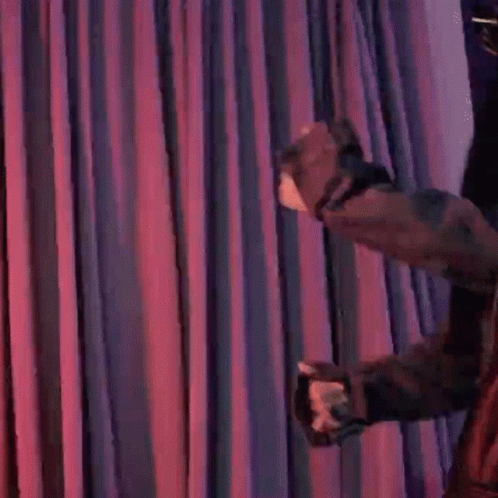 A Woman Is Standing In Front Of A Purple Curtain Holding A Microphone And Blowing A Kiss . GIF