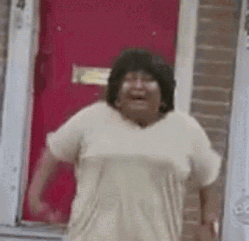 A Woman Is Standing In Front Of A Red Door Laughing . GIF