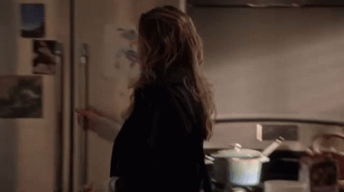 A Woman Is Standing In Front Of A Refrigerator In A Kitchen . GIF