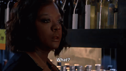 A Woman Is Standing In Front Of A Shelf With Wine Bottles And Says What . GIF