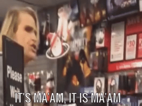 A Woman Is Standing In Front Of A Sign That Says Please Wait It 'S Ma 'Am It Is Ma 'Am GIF