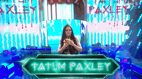 A Woman Is Standing In Front Of A Sign That Says Tatum Paxley On It . GIF