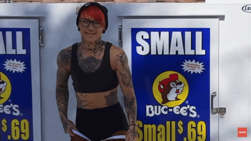 A Woman Is Standing In Front Of A Small Buck-Ee 'S Sign GIF