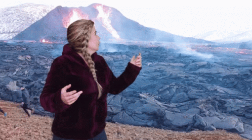 A Woman Is Standing In Front Of A Volcano GIF
