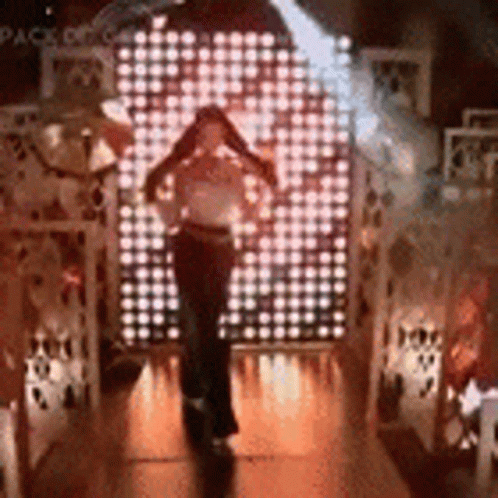 A Woman Is Standing In Front Of A Wall Of Lights In A Dark Room . GIF