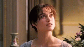 A Woman Is Standing In Front Of A Window In A Room With A Vase In The Background . GIF