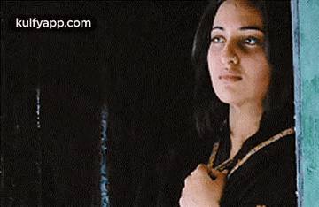 A Woman Is Standing In Front Of A Window Looking Out . GIF