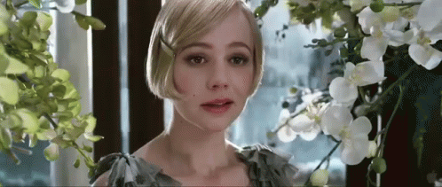 A Woman Is Standing In Front Of A Window Surrounded By Flowers And Looking At The Camera . GIF