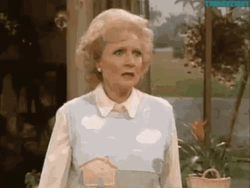 A Woman Is Standing In Front Of A Window Wearing A Blue Sweater With Clouds On It . GIF