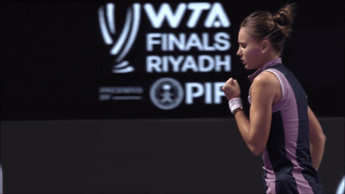 A Woman Is Standing In Front Of A Wta Finals Riyadh Sign GIF