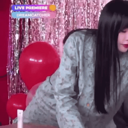 A Woman Is Standing In Front Of Balloons And A Live Premiere Sign GIF