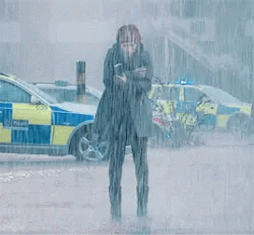 A Woman Is Standing In The Rain In Front Of A Police Car Holding A Cell Phone . GIF