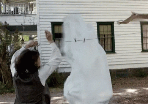 A Woman Is Standing Next To A Ghost Hanging On A Clothes Line In Front Of A White House . GIF
