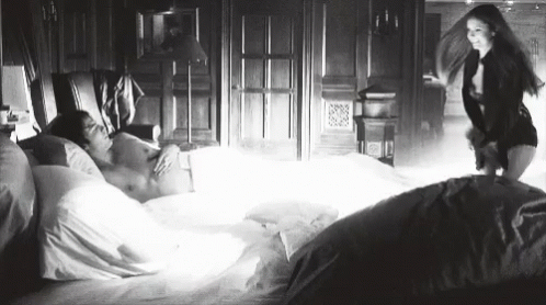 A Woman Is Standing Next To A Man In A Bed . GIF