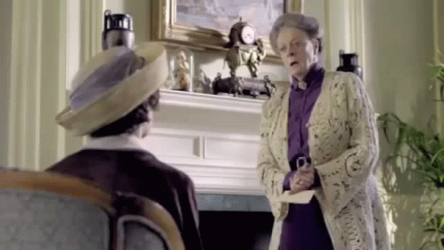 A Woman Is Standing Next To A Man In A Living Room Holding A Piece Of Paper . GIF