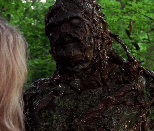 A Woman Is Standing Next To A Statue Of A Monster Covered In Mud GIF