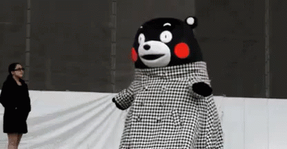 A Woman Is Standing Next To A Teddy Bear Wearing A Black And White Plaid Coat . GIF