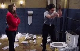 A Woman Is Standing Next To A Toilet In A Messy Bathroom . GIF