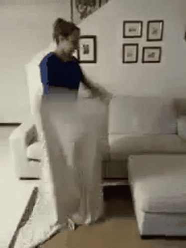 A Woman Is Standing Next To A White Couch In A Living Room GIF