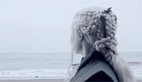 A Woman Is Standing On A Beach Looking At The Ocean . GIF
