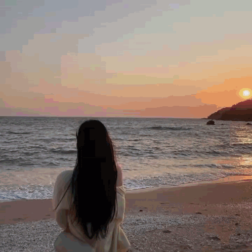 A Woman Is Standing On A Beach Looking At The Ocean GIF