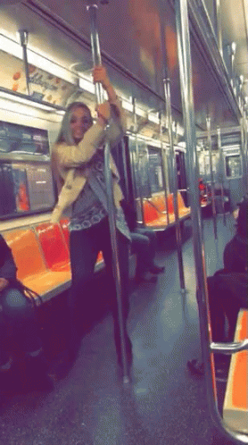 A Woman Is Standing On A Pole In A Subway Car GIF