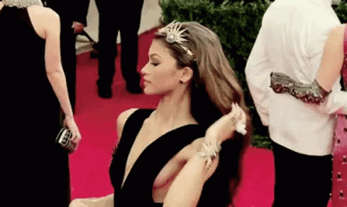 A Woman Is Standing On A Red Carpet Adjusting Her Hair . GIF