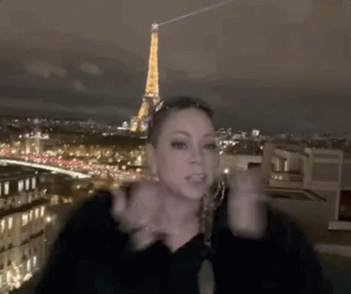 A Woman Is Standing On A Rooftop In Front Of The Eiffel Tower At Night . GIF