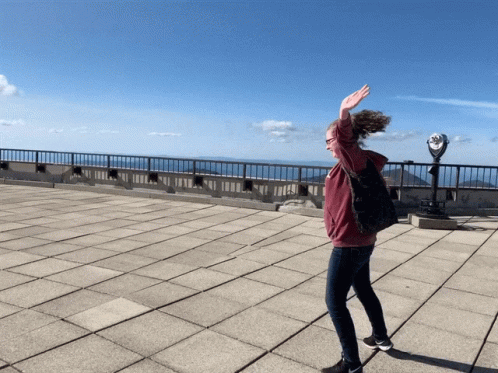 A Woman Is Standing On A Rooftop With Her Arms Outstretched GIF
