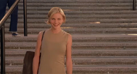 A Woman Is Standing On A Set Of Stairs Smiling And Holding A Bag . GIF