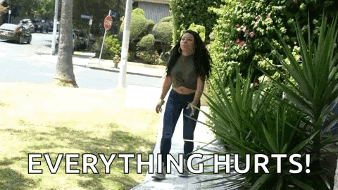 A Woman Is Standing On A Sidewalk With The Words `` Everything Hurts '' Written On The Ground . GIF