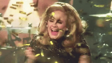 A Woman Is Standing On A Stage Surrounded By Confetti And Laughing . GIF