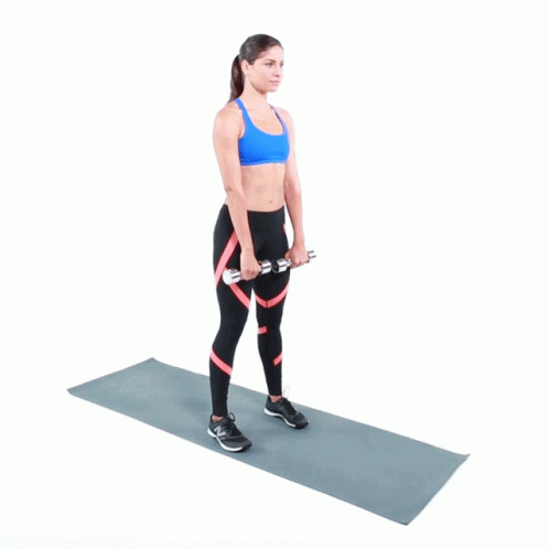 A Woman Is Standing On A Yoga Mat Holding Two Dumbbells In Her Hands GIF