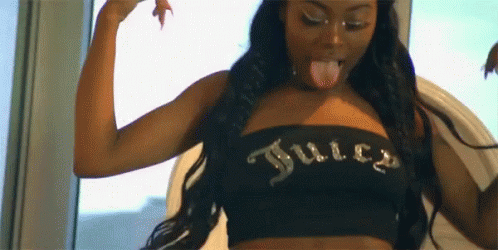 A Woman Is Sticking Her Tongue Out While Wearing A Black Juicy Couture Top . GIF