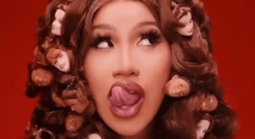 A Woman Is Sticking Her Tongue Out While Wearing A Wig With Heads On It . GIF