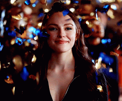 A Woman Is Surrounded By Blue And Gold Confetti And Is Smiling . GIF