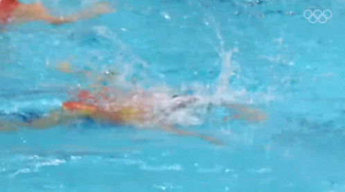 A Woman Is Swimming In A Pool With The Olympic Rings Visible In The Background GIF