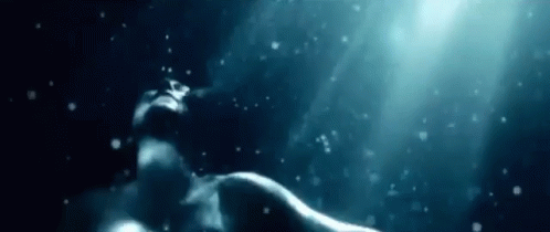 A Woman Is Swimming Underwater In The Ocean With Bubbles Coming Out Of Her Mouth . GIF