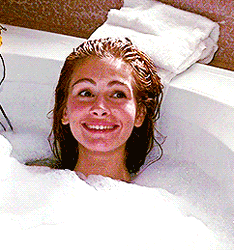 A Woman Is Taking A Bath In A Bathtub And Smiling GIF