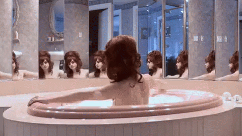 A Woman Is Taking A Bath In A Jacuzzi In Front Of A Mirror . GIF