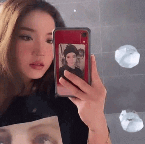 A Woman Is Taking A Picture Of Herself In A Mirror With Her Phone . GIF
